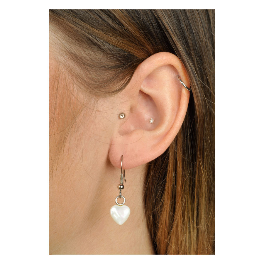 Weiße herzförmige Ohrringe aus Silber an einem Ohr mit braunem Haar