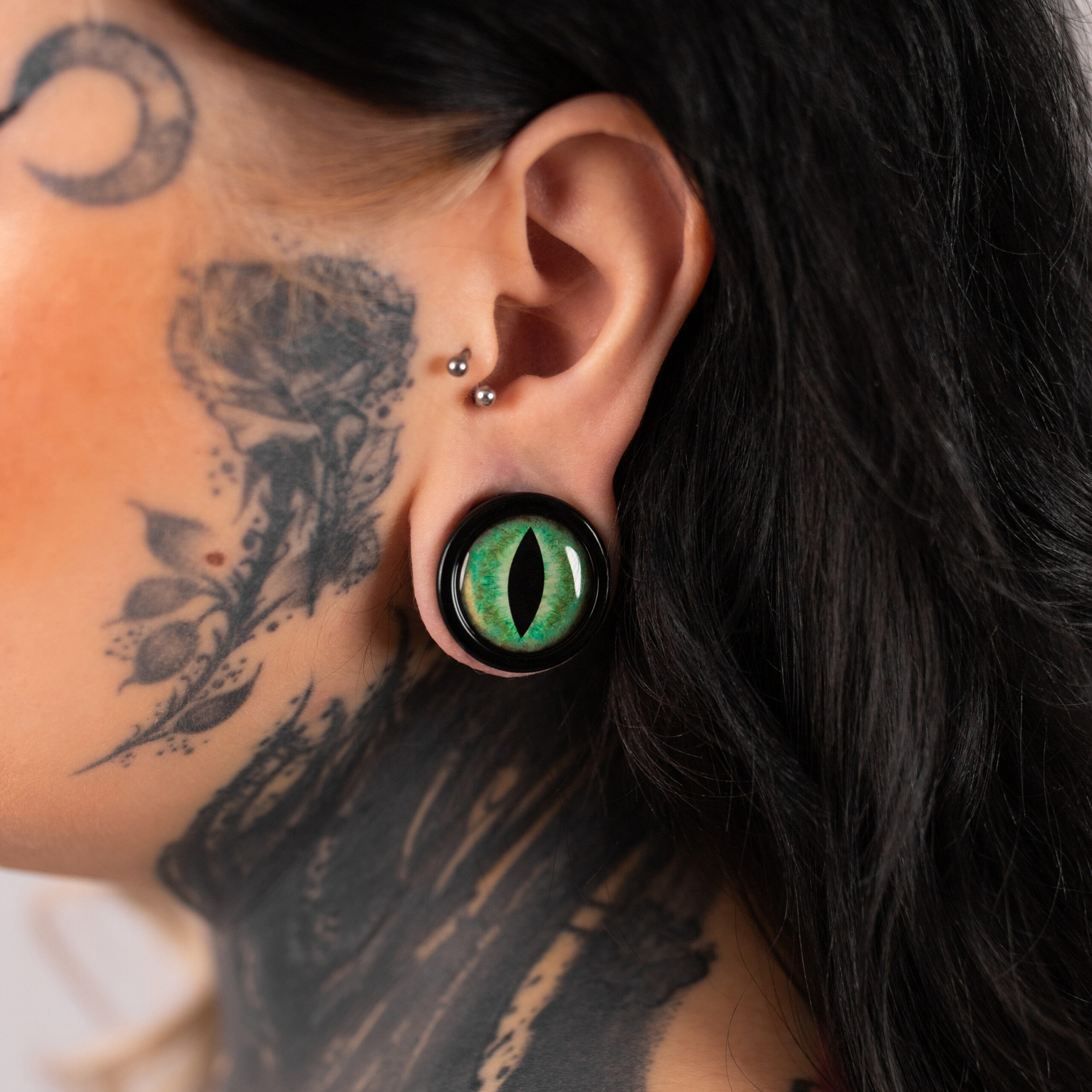 Großer grüner Katzenaugen-Plug im Ohr einer tätowierten Person