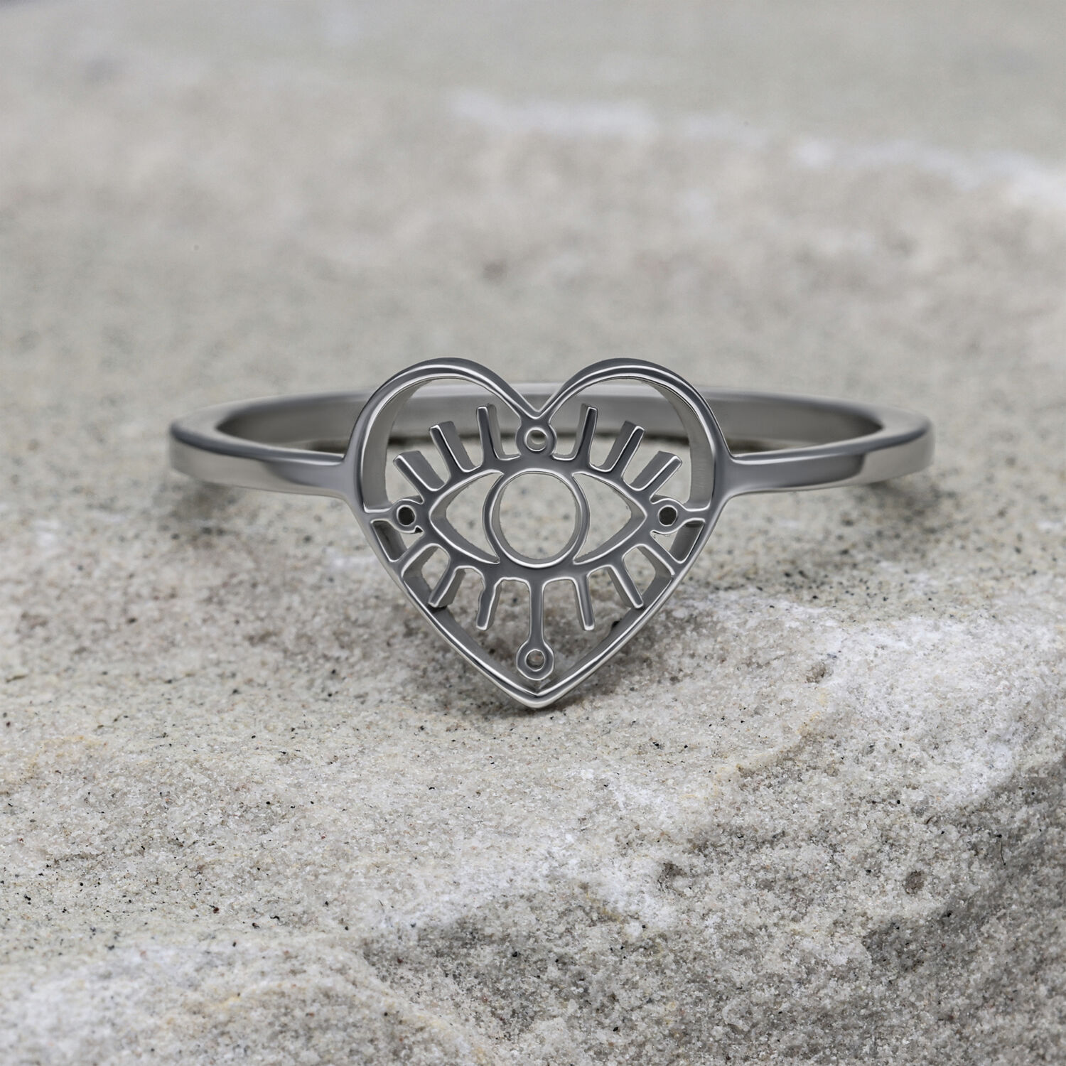 Silberner herzförmiger Ring mit Auge-Motiv auf grauem Stein