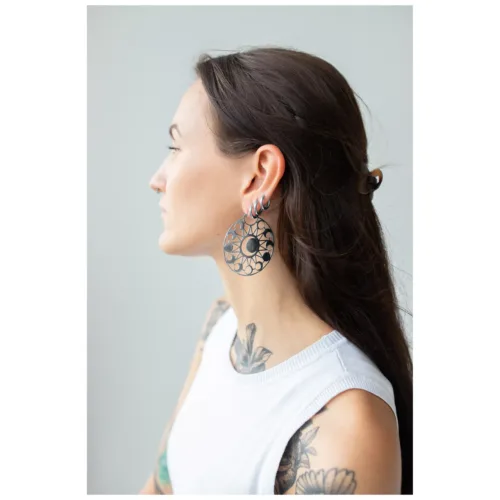 Frau mit langen dunklen Haaren trägt große, runde Ohrringe mit Mondmuster vor grauem Hintergrund