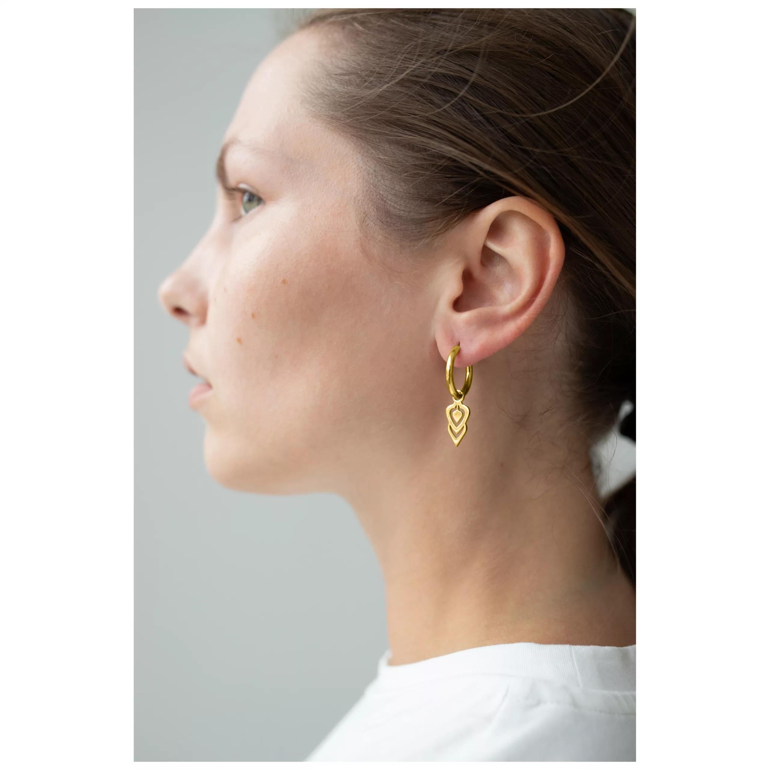 Frau mit goldenen Little Balisuta Hoops Ohrringen vor neutralem Hintergrund