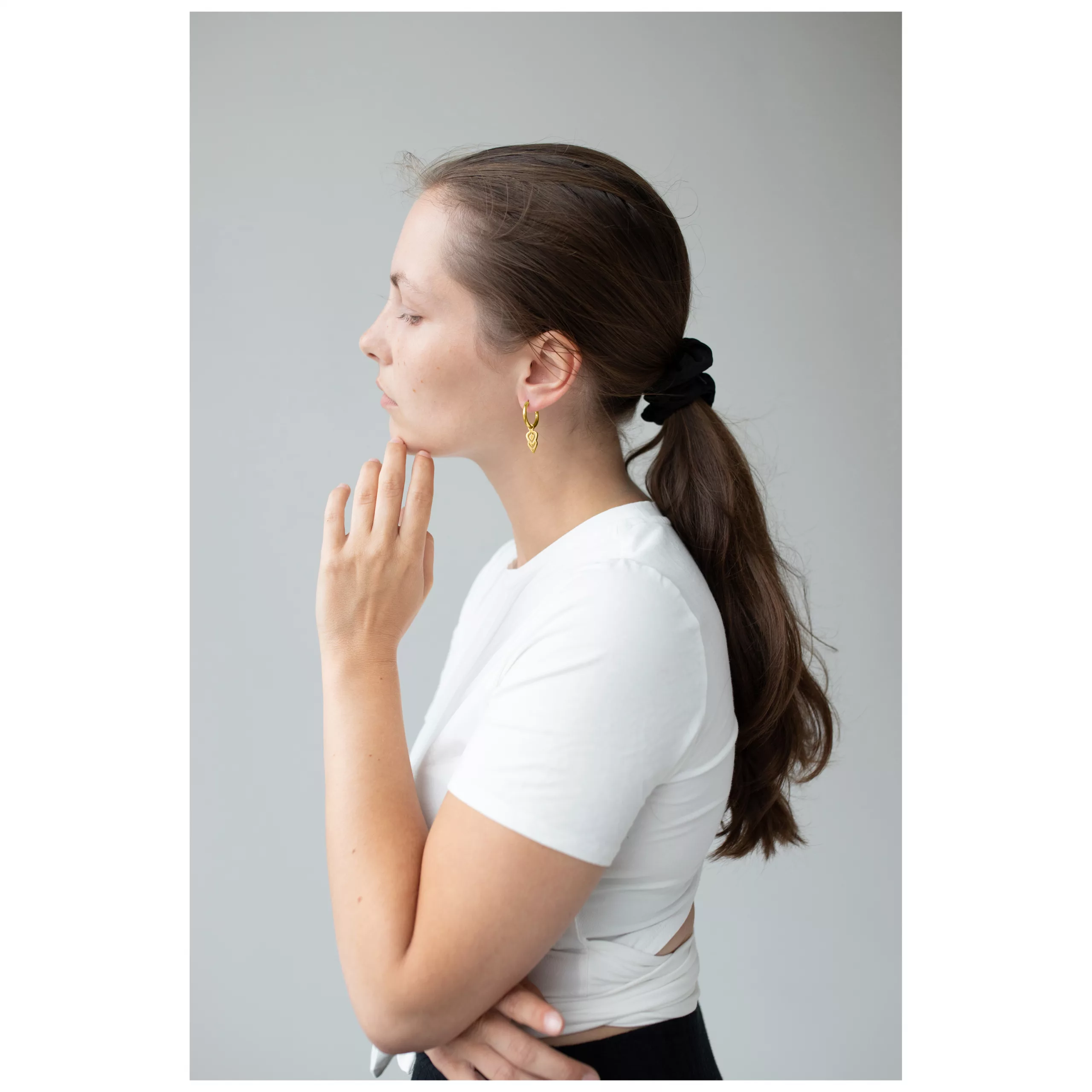 Frau mit langen Haaren trägt goldene Hoops Ohrringe vor grauem Hintergrund