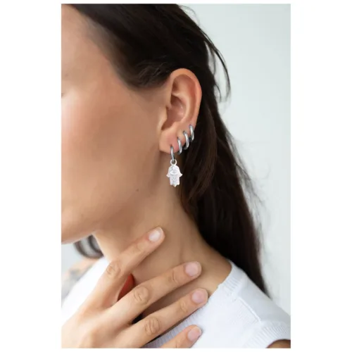 Nahaufnahme einer Frau mit silbernen Little Hamsa Hand Hoops Ohrringen, die ihr Ohr schmücken