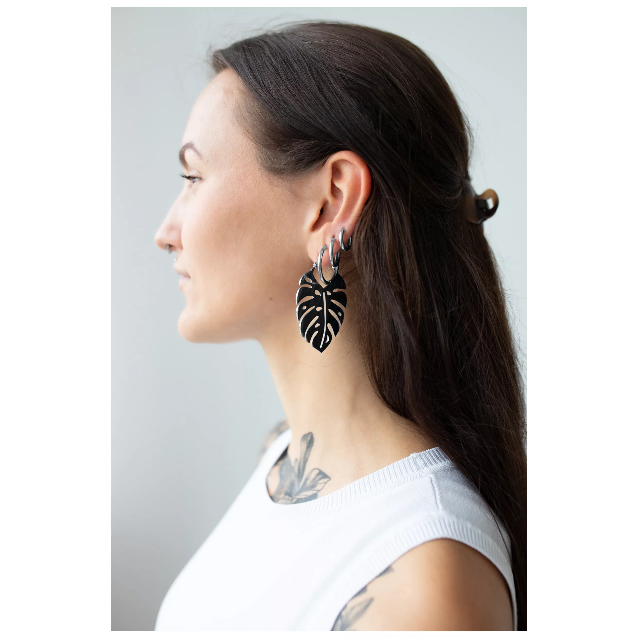 Monstera Leaf Hoops in Schwarz und Silber Frau mit Monstera-Ohrringen in Schwarz und Silber vor hellem Hintergrund