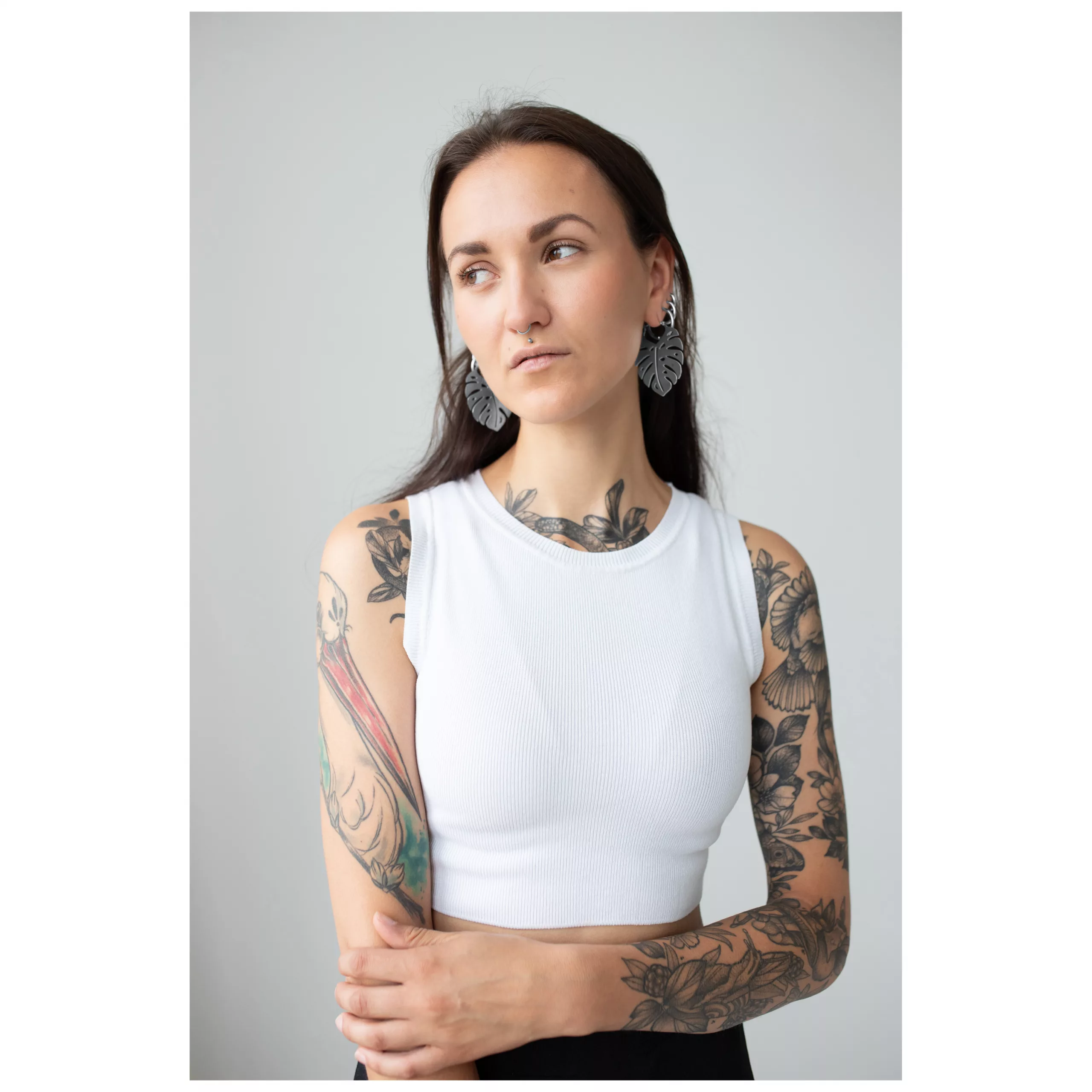 Monstera Leaf Hoops mit Frau im Studio Frau mit tätowierten Armen trägt Monstera Leaf Hoops Ohrringe, weißes Top