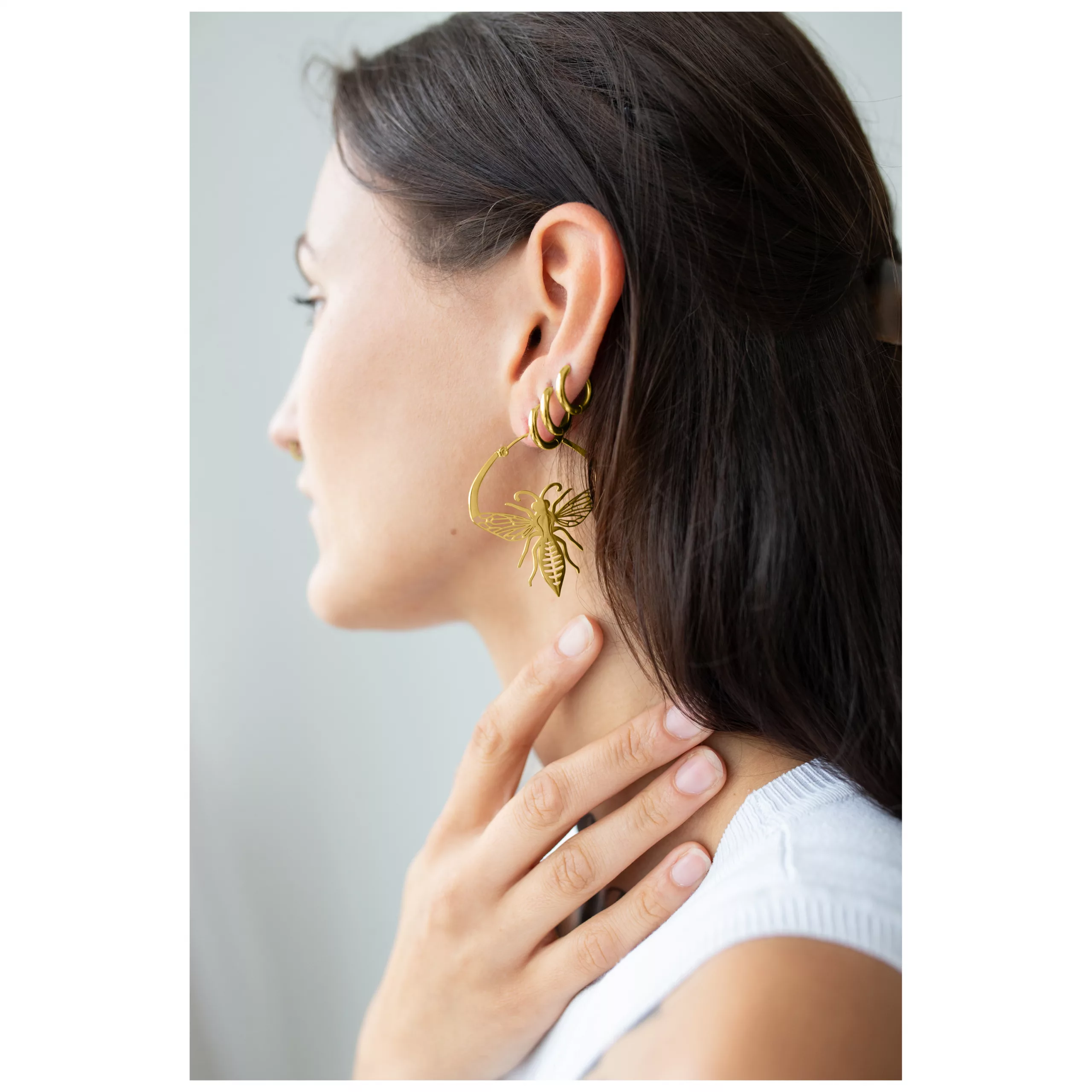 Frau mit goldenen Bienen-Ohrringen aus Chirurgenstahl vor neutralem Hintergrund