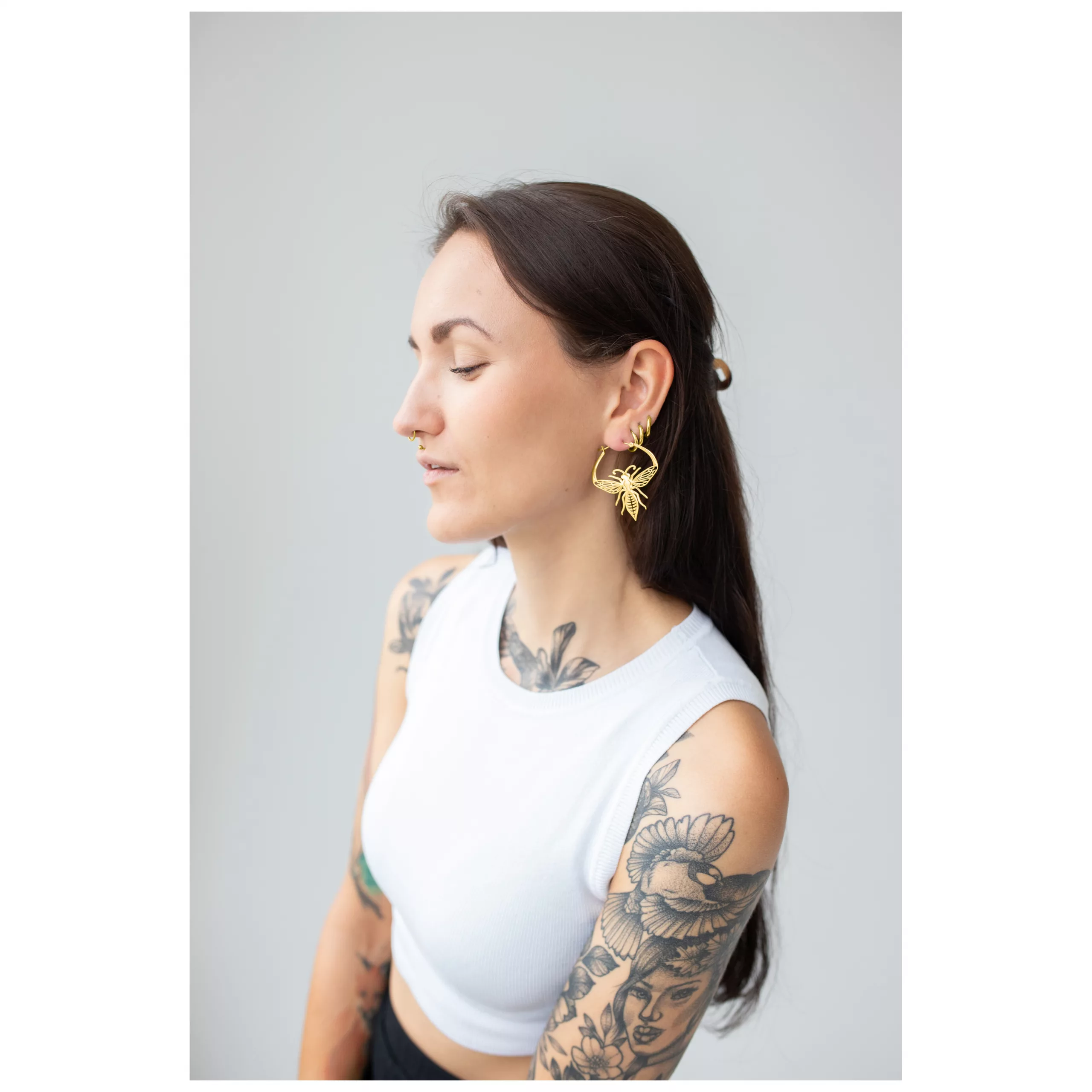 Frau mit langen Haaren trägt goldene Bee Hoops Ohrringe aus Chirurgenstahl vor grauem Hintergrund