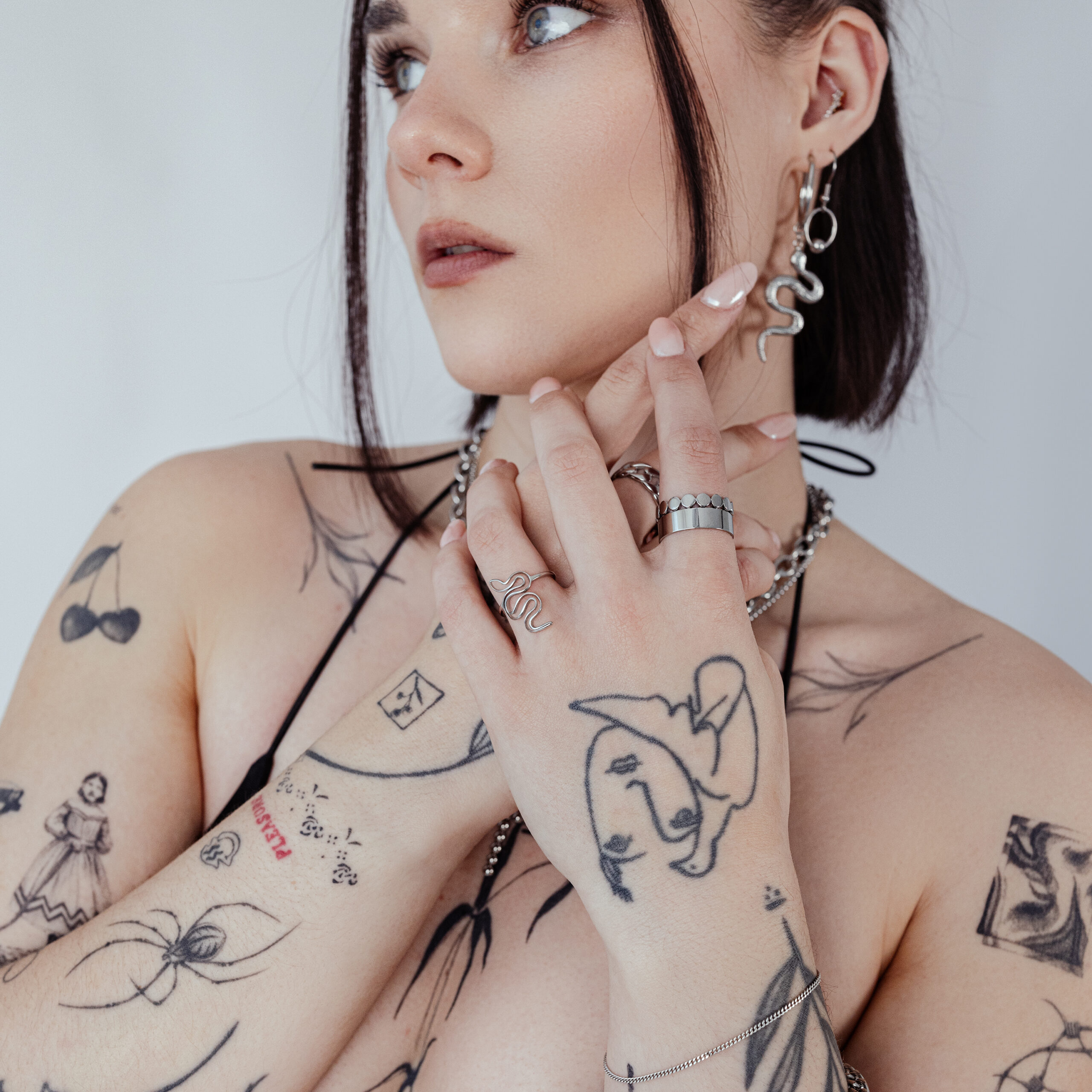 Person mit Schlangenring und Tattoos, trägt Schmuck auf weißem Hintergrund