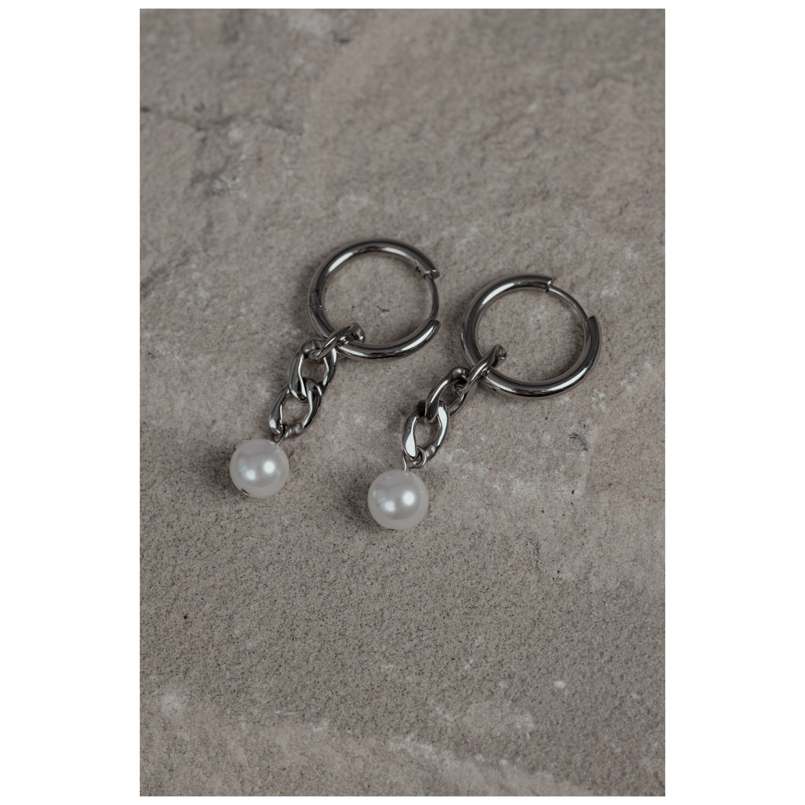 Silberne Creolen mit Perlenanhänger Zwei silberne Creolen mit kleinen Perlenanhängern auf grauem Stein