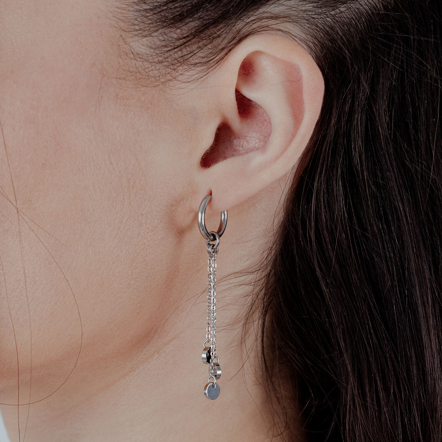 Silberne Creolen mit Kettenanhänger an weiblichem Ohr vor hellem Hintergrund