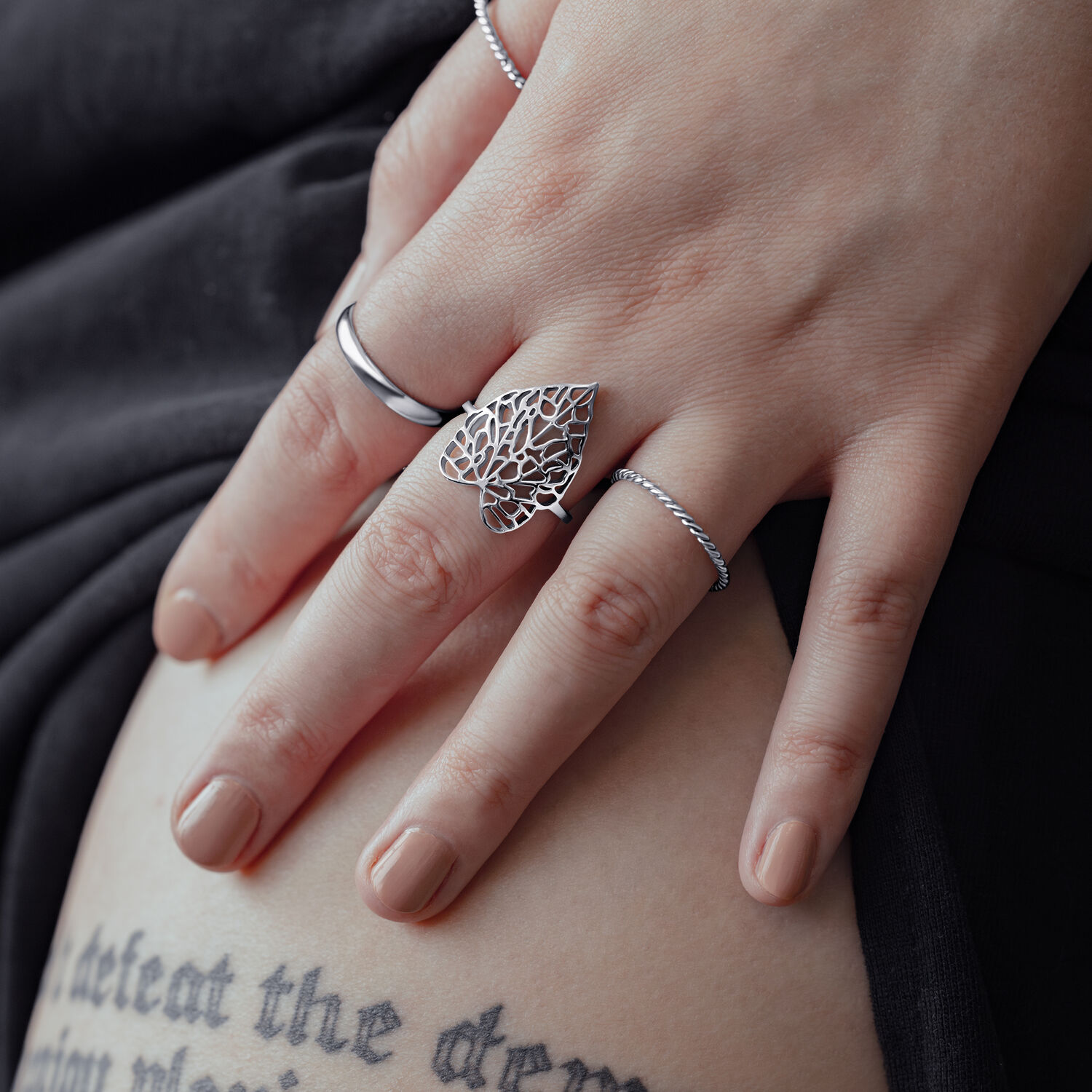 Silberner Ring im Blattdesign an weiblicher Hand auf schwarzem Hintergrund