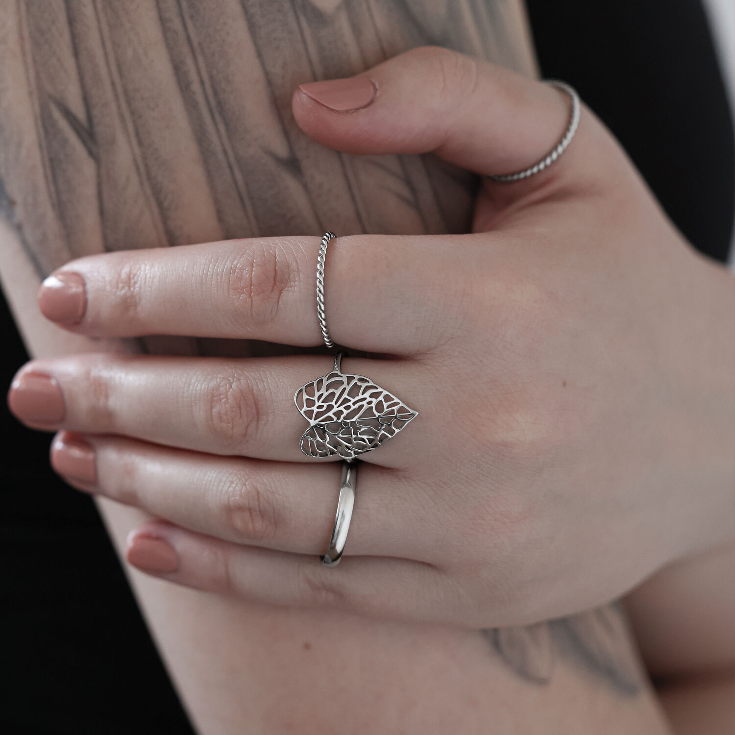 Silberner Blatt-Ring aus Chirurgenstahl auf einer tätowierten Hand vor hellem Hintergrund