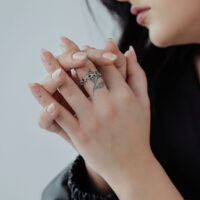 Silberner Kettenglied-Ring an den Händen einer Person mit tätowierten Fingern und schwarzen Ärmeln