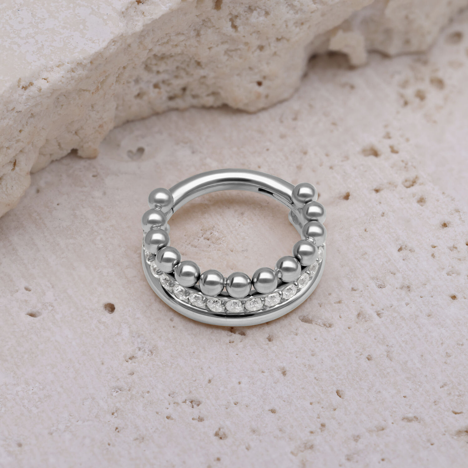 Silberner Triple Bubble Clicker mit weißen Kristallen auf beigem Stein