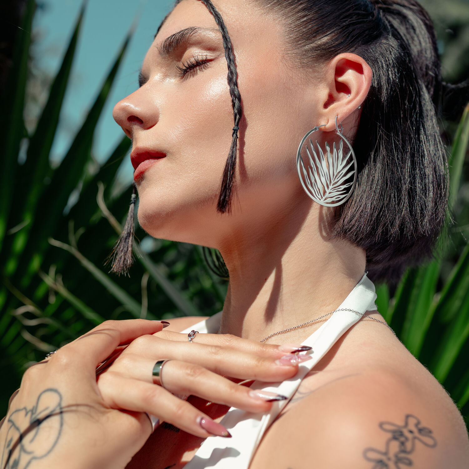 Frau mit großen silbernen Ohrringen vor grüner Pflanze