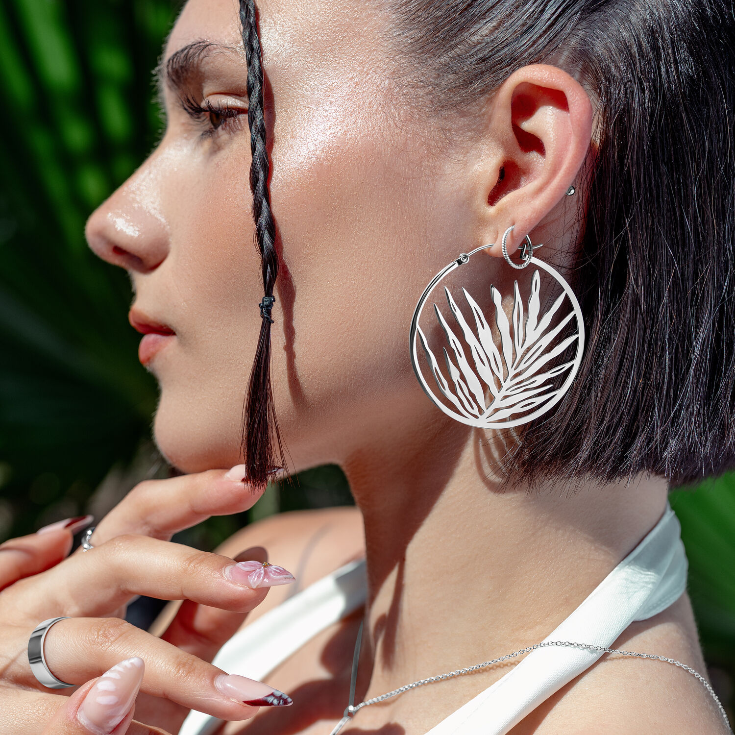 Silberne Noble Leaf Hoops Ohrringe an Frau mit geflochtenem Haar und tropischem Hintergrund