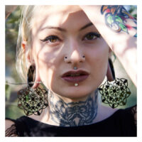 Frau mit großen schwarzen floralen Ohrringen aus Chirurgenstahl