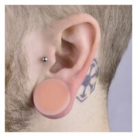 Kaos Softwear Hider Plug in Hautfarbe, Größe 6,0 mm, im Ohr eines Mannes mit Tattoo und Piercing.