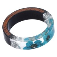 Transparenter Harzring mit blauer Blume und Holzeinlage auf weißem Hintergrund