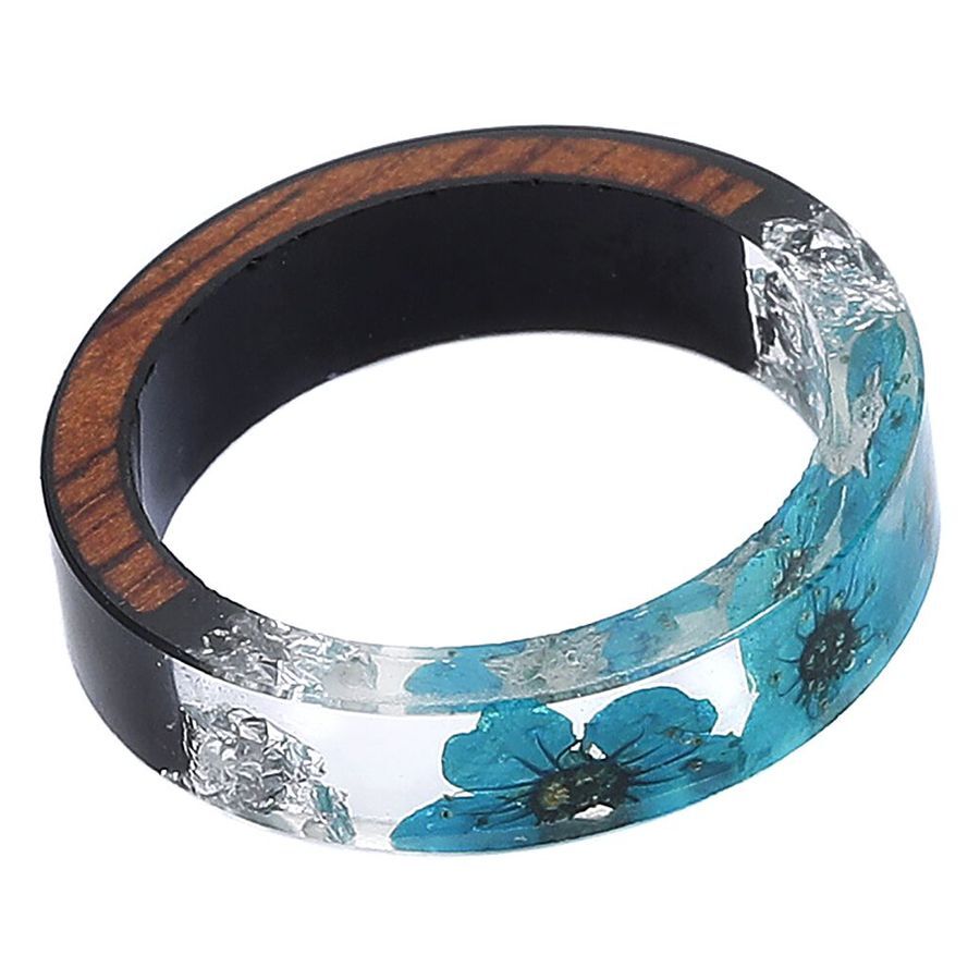 Transparenter Harzring mit blauer Blume und Holzeinlage auf weißem Hintergrund