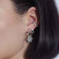 Silberner Kristall-Anhänger am Ohr mit weiteren Piercings auf weißem Hintergrund