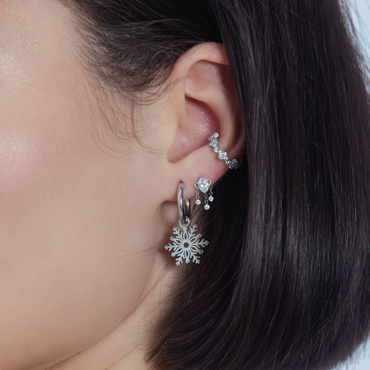 Silberner Kristall-Anhänger am Ohr mit weiteren Piercings auf weißem Hintergrund