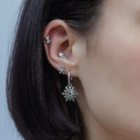 Ohr mit mehreren silbernen Piercings, Schneeflocken-Design, auf neutralem Hintergrund