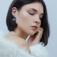 Frau mit silbernem Schneeflocken-Piercing im Ohr vor hellem Hintergrund