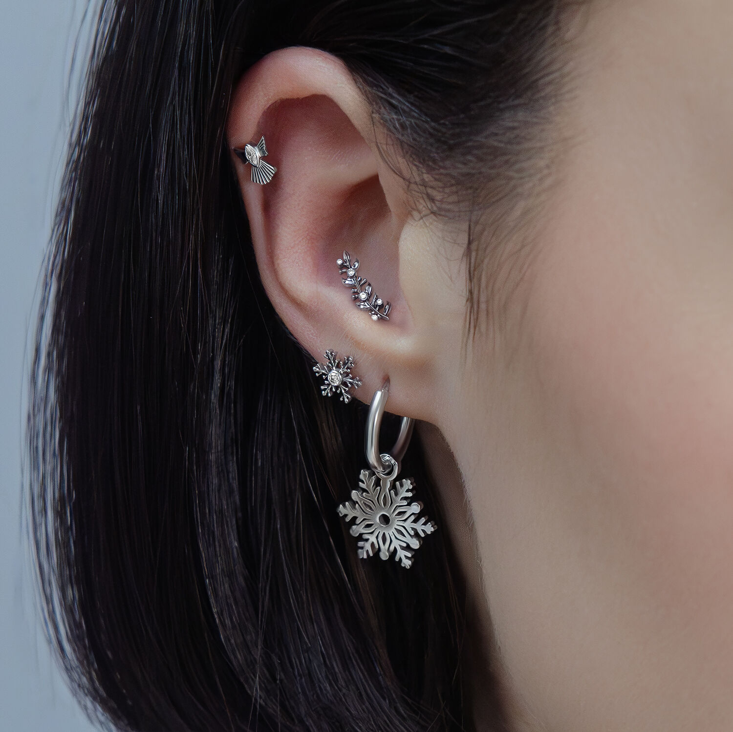 Nahaufnahme eines Ohrs mit mehreren silbernen Piercings in verschiedenen Designs und Kristallen