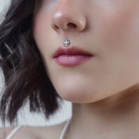 Nahaufnahme eines silbernen Kristall-Piercing-Aufsatzes am Medusa-Piercing einer Frau auf neutralem Hintergrund