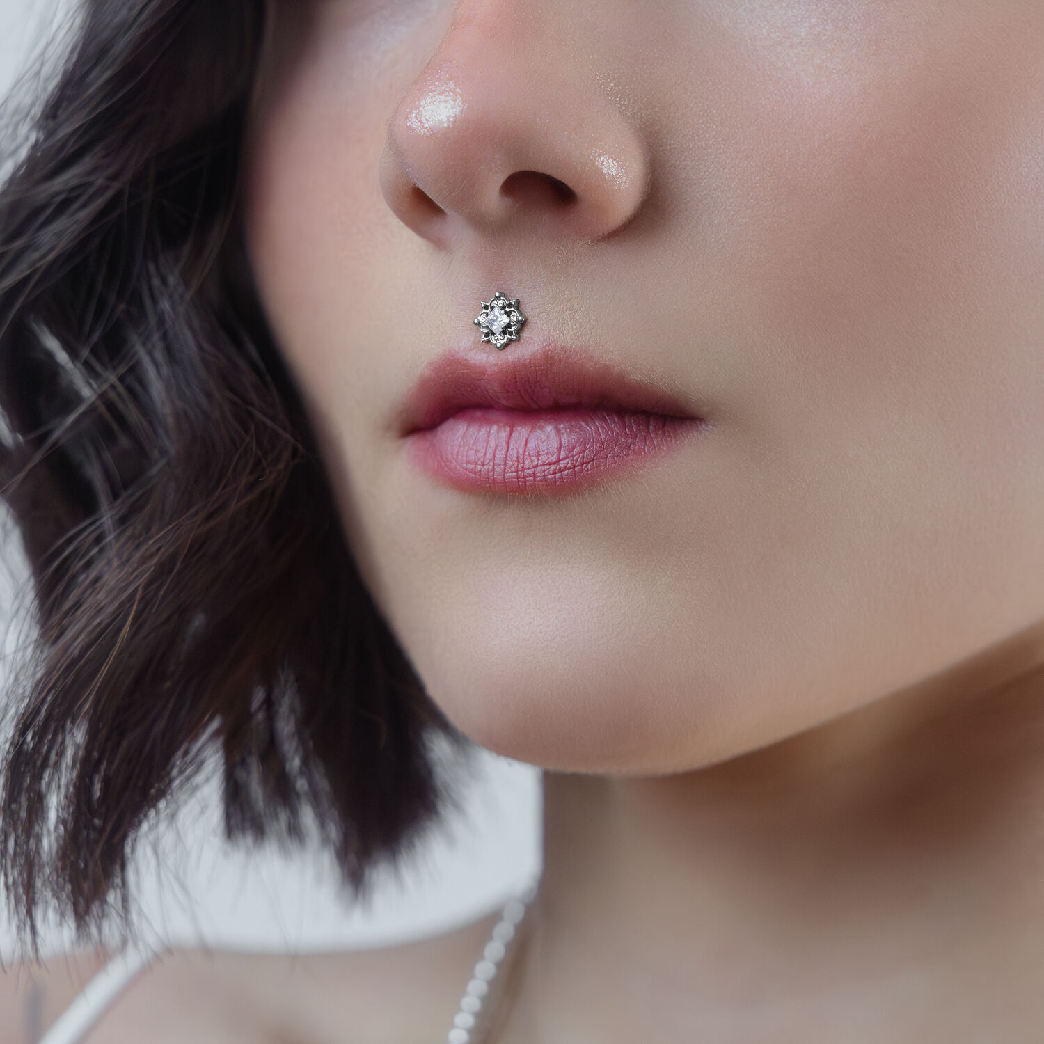 Nahaufnahme eines silbernen Kristall-Piercing-Aufsatzes am Medusa-Piercing einer Frau auf neutralem Hintergrund