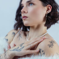 Frau mit Ice Flower Kristallaufsatz im Ohr, silberne Farbe, vor neutralem Hintergrund