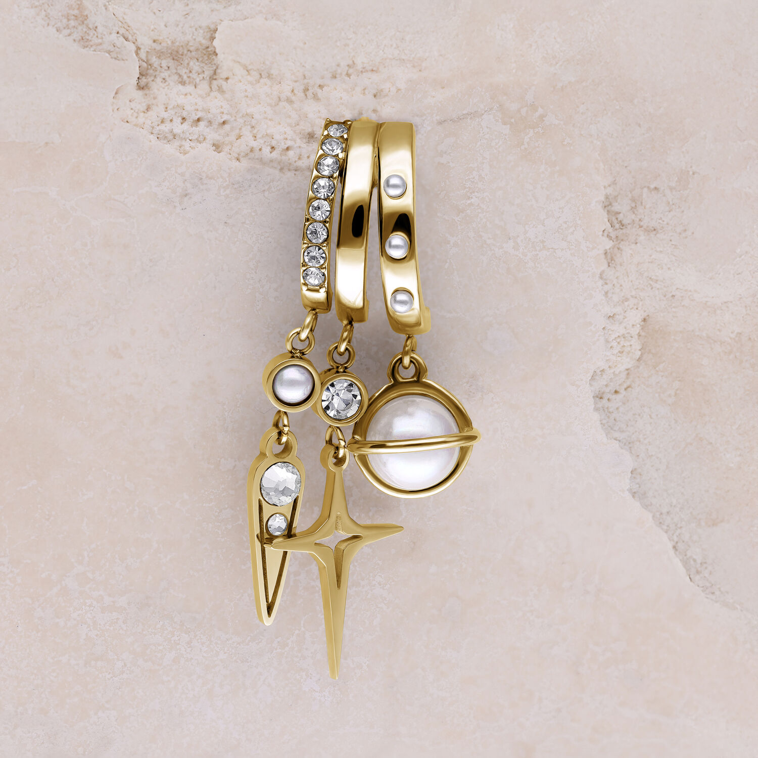 Drei goldene Ohrstecker mit Perlen, Glitzersteinen und Sternanhänger auf beigem Hintergrund