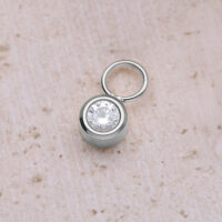 Runder Kristallanhänger aus Chirurgenstahl Silberner runder Kristallanhänger aus Chirurgenstahl auf beigem Hintergrund