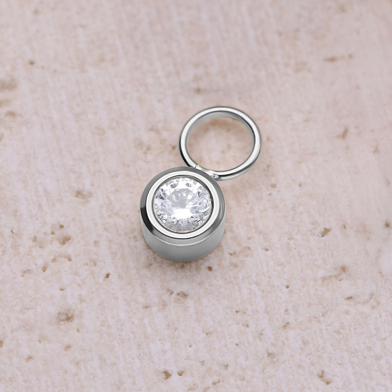 Runder Kristallanhänger aus Chirurgenstahl Silberner runder Kristallanhänger aus Chirurgenstahl auf beigem Hintergrund
